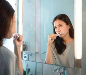 a woman brushing her teeth in the mirror