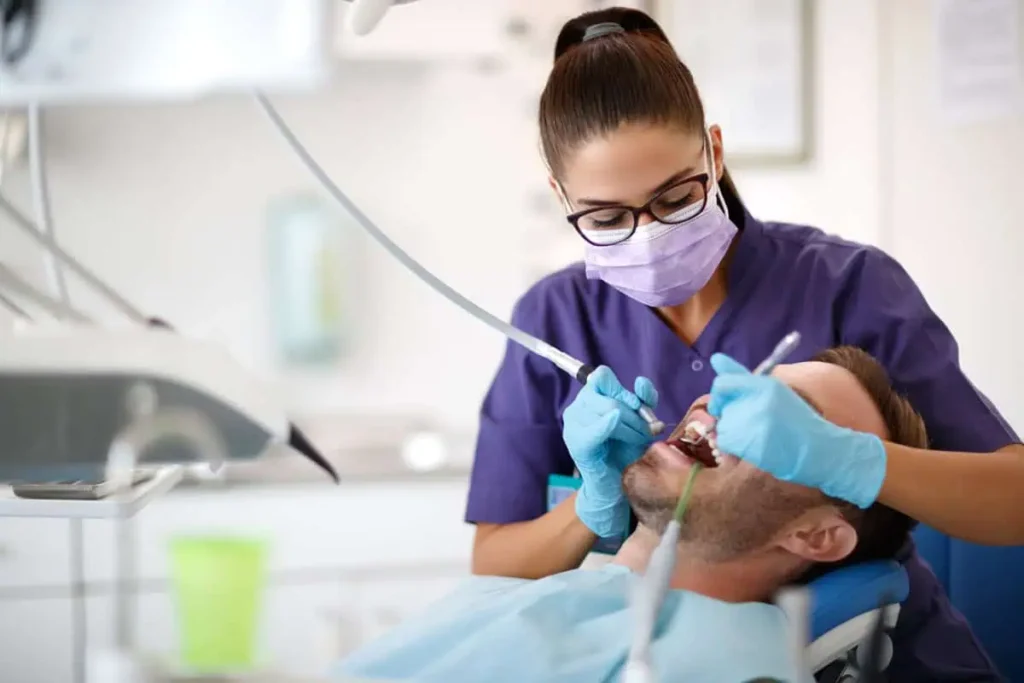 a woman in purple scrubs and gloves holding tools to a man's mouth