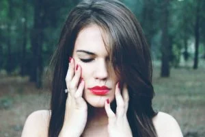 a woman with red lipstick and red nails touching her face