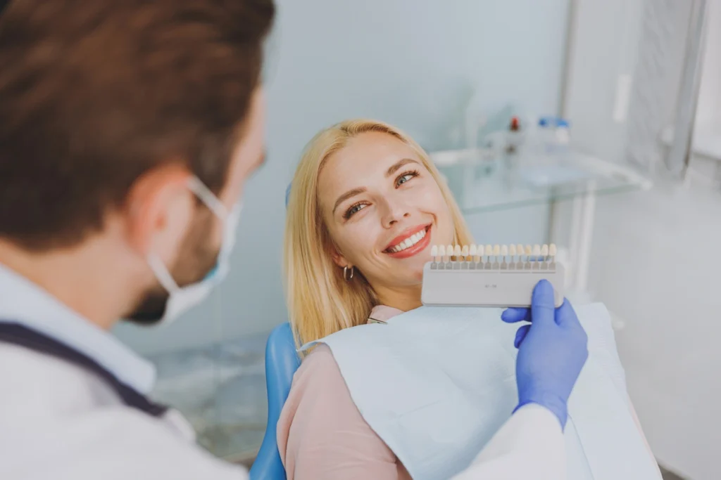 a woman sitting in a chair with a dentist holding a color chart
