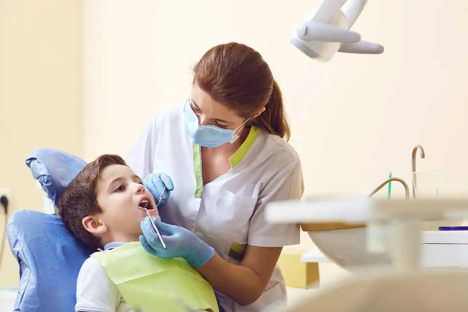 a woman in a white coat and blue gloves examining a boy's teeth