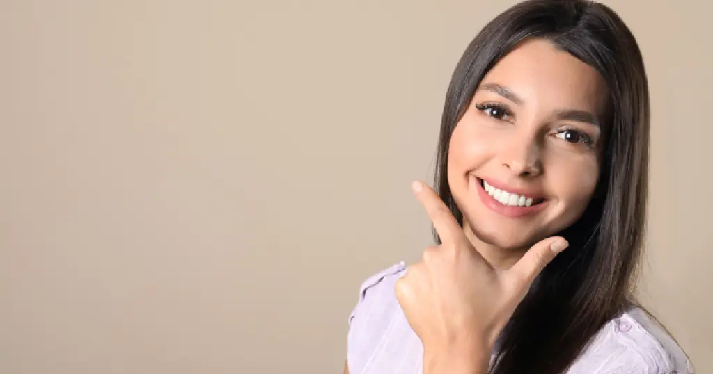 Smiling woman with straight dark hair pointing to her teeth, showcasing a bright and symmetrical smile after tooth contouring in Harrisburg, NC.